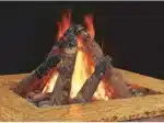 Campfire with logs arranged in a teepee on sandy ground, flames rising.