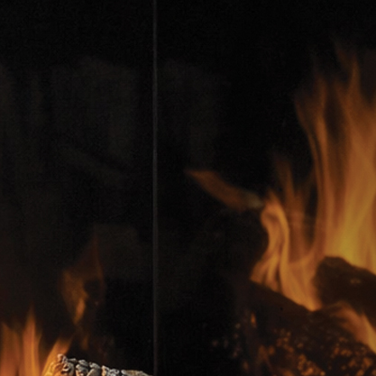 Close-up of a blazing fire with orange flames licking logs in a dark fireplace.